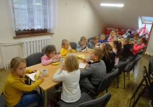 Grupa dzieci siedzi przy stole i je ciasto.